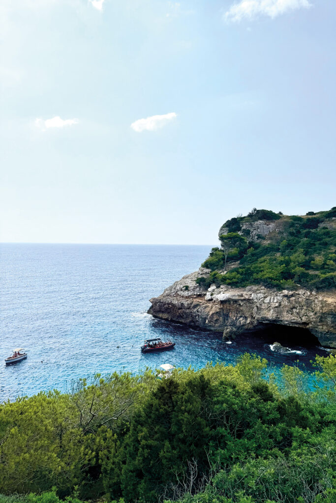 Felsige Bucht auf Mallorca mit türkisblauem Meer und Ausflugsbooten.