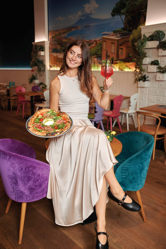 Elegante Mode mit hellem Satinrock beim Restaurantbesuch mit Pizza und Cocktail.