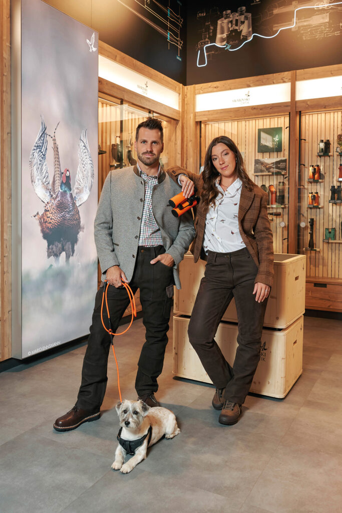 Mode im Jagdstil: Frau und Mann in herbstlichen Outfits mit Hund und Fernglas.