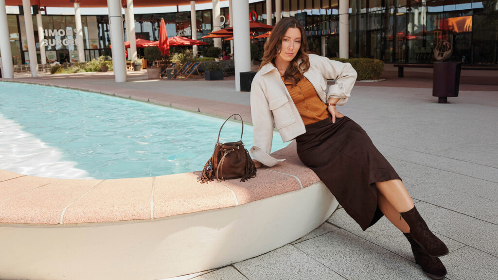 Herbstliche Mode mit braunem Maxirock, heller Jacke, Stiefeln und passender Handtasche.
