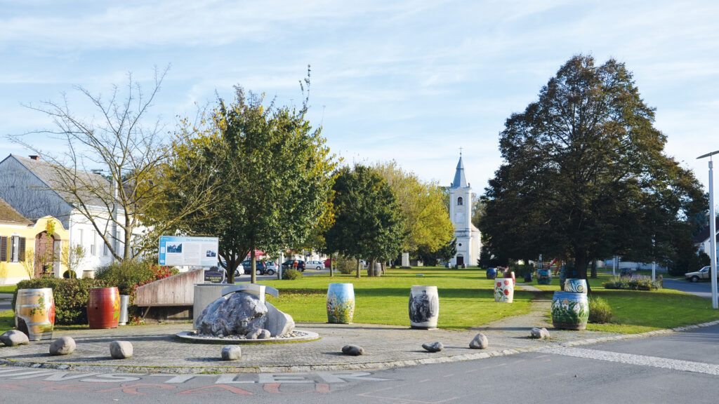 Eberau im Burgenland: Hauptplatz mit Parkanlage, Kirche und bunt gestalteten Weinfässern.