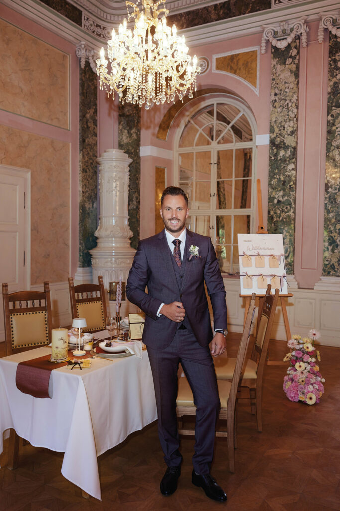 Hochzeitsshooting mit Bräutigam im eleganten Festsaal mit festlich gedecktem Tisch und Kronleuchter