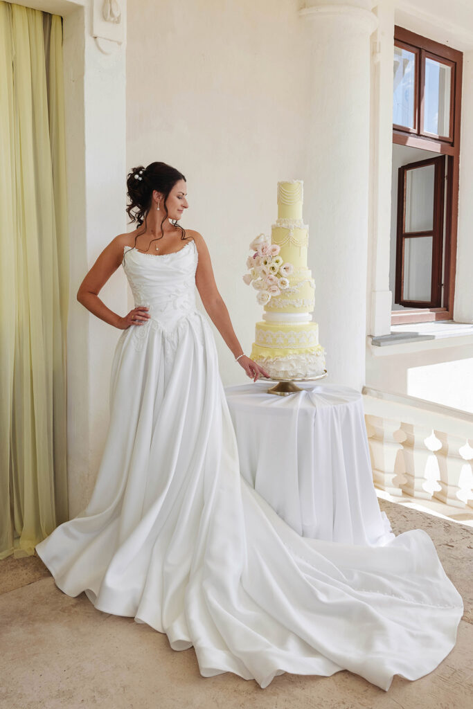 Hochzeitsshooting mit Braut im eleganten weißen Hochzeitskleid neben einer mehrstöckigen Hochzeitstorte