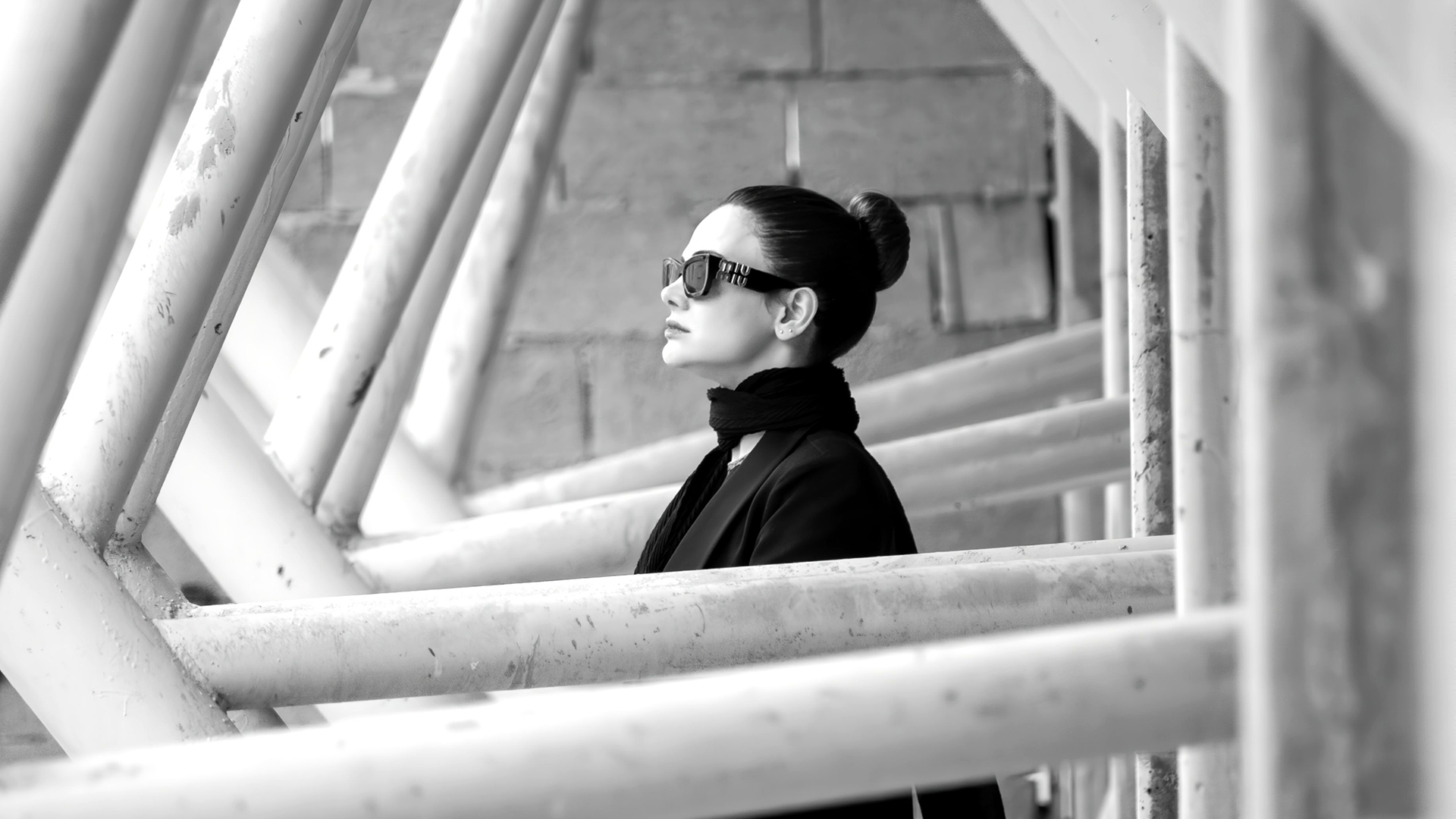 Oktober: Frau mit Sonnenbrille in einer Schwarz-Weiß-Aufnahme zwischen markanten Stahlträgern.