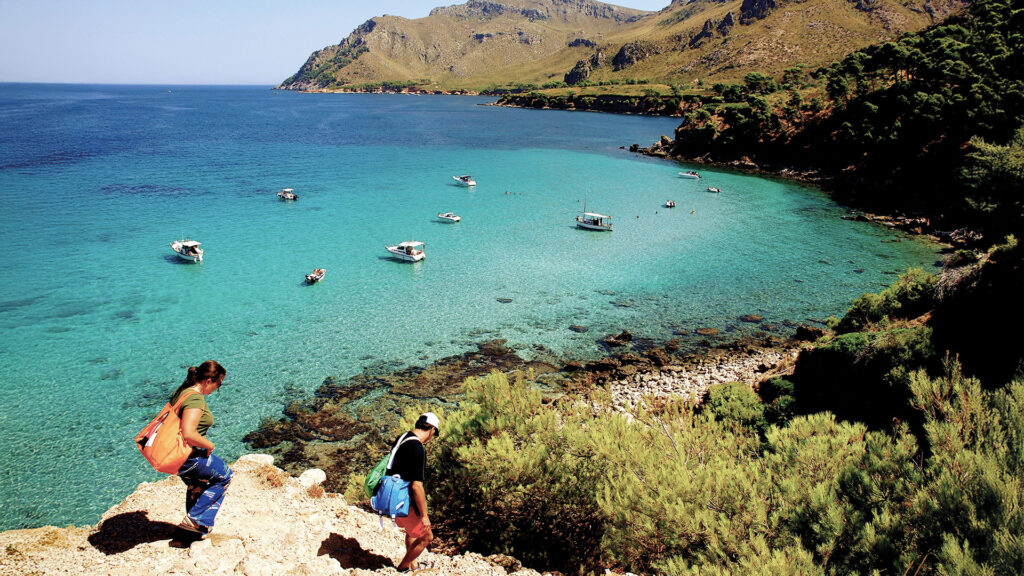 Naturbucht auf Mallorca mit kristallklarem Wasser, Booten und felsiger Küstenlandschaft.