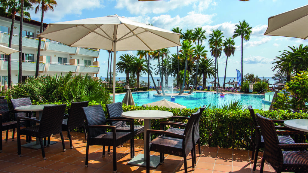 Hotel auf Mallorca mit Terrasse, Pool, Palmen und Blick Richtung Meer.