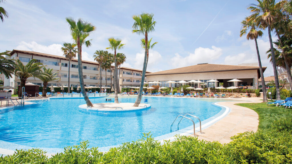 Hotelpool auf Mallorca mit Palmen und mediterraner Ferienanlage.