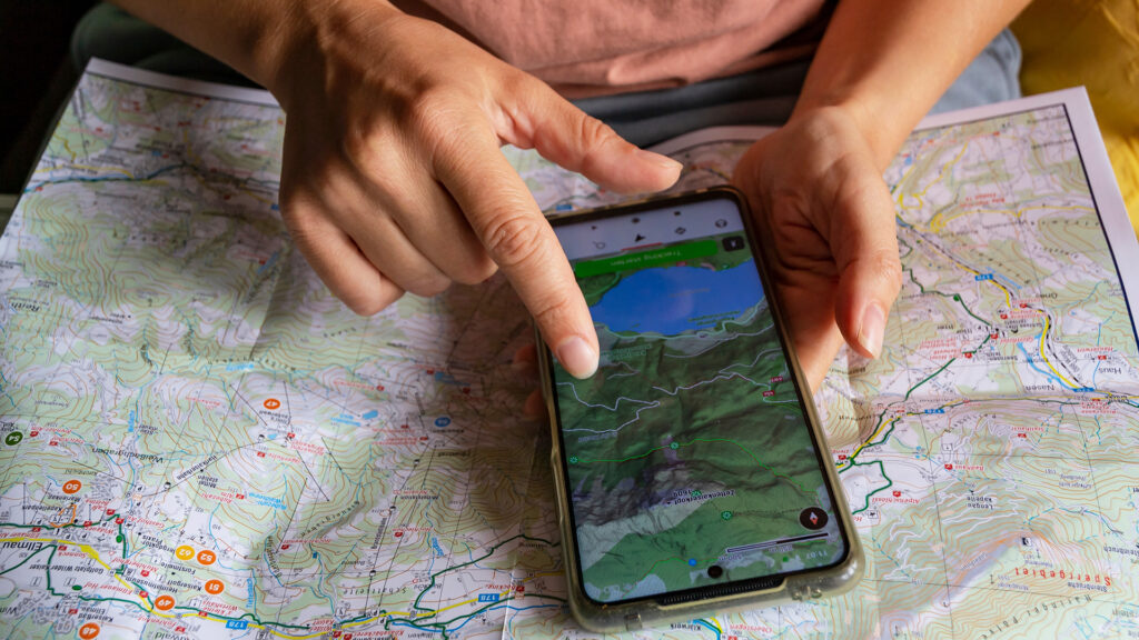 Alleinreisen mit guter Planung: Smartphone mit digitaler Karte auf einer Wanderkarte.