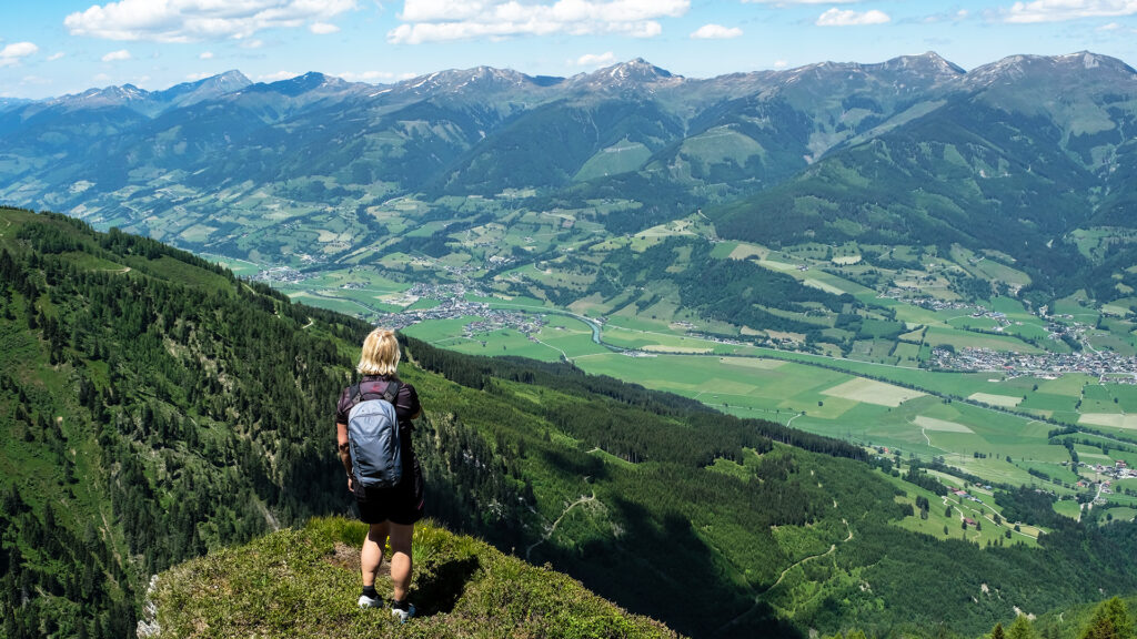 Alleinreisen in Zell am See: Wanderin mit Rucksack blickt über das Tal und die österreichischen Alpen.