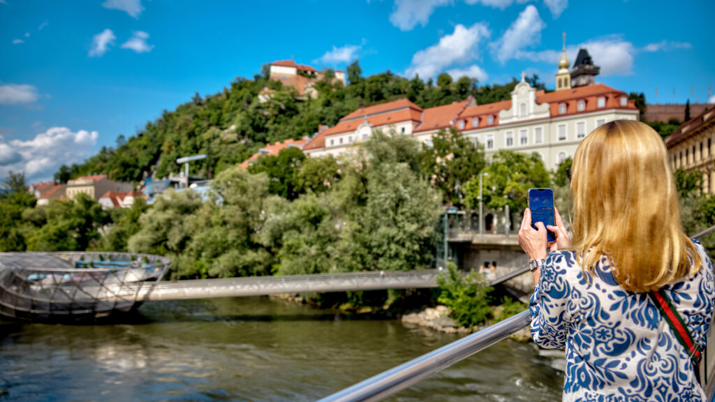 Alleinreisen in Graz: Frau fotografiert die Grazer Altstadt und den Schlossberg mit dem Smartphone.