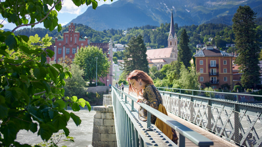 Alleinreisen in Innsbruck: Frau auf einer Brücke vor historischer Stadtkulisse und Tiroler Bergen.