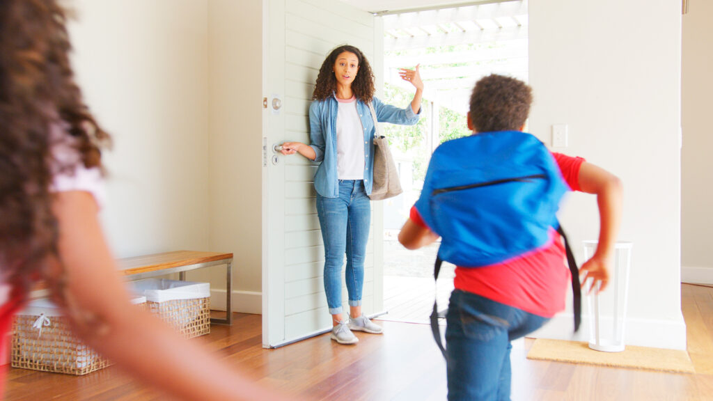 Schulstart nach den Ferien: Kinder mit Rucksäcken verlassen morgens das Haus und verabschieden sich von ihrer Mutter