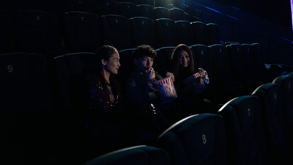 Kino: 3 Personen sitzen im Kino und essen Popcorn