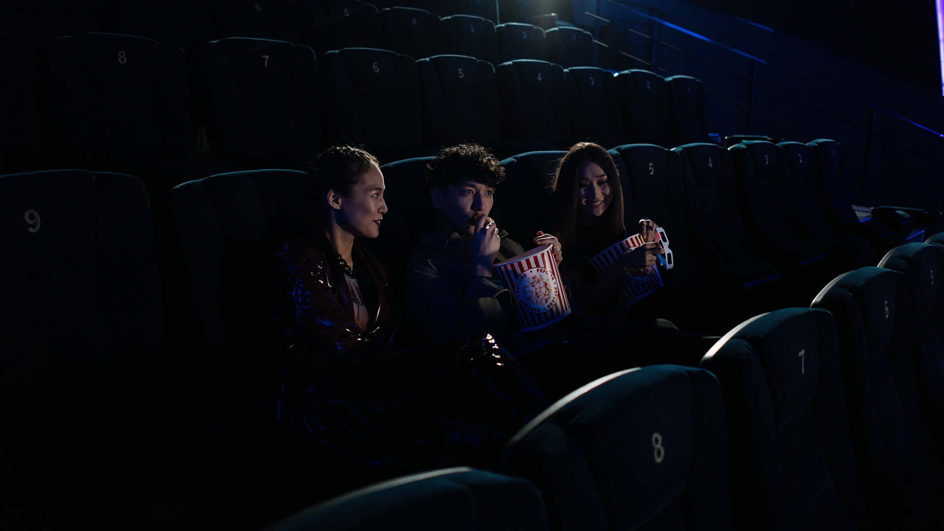 Kino: 3 Personen sitzen im Kino und essen Popcorn